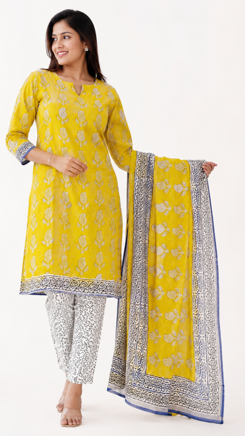 A woman models a yellow ethnic suit set featuring a kurta with floral prints, silver patterned pants, and a matching dupatta with a blue border, set against a plain white background.