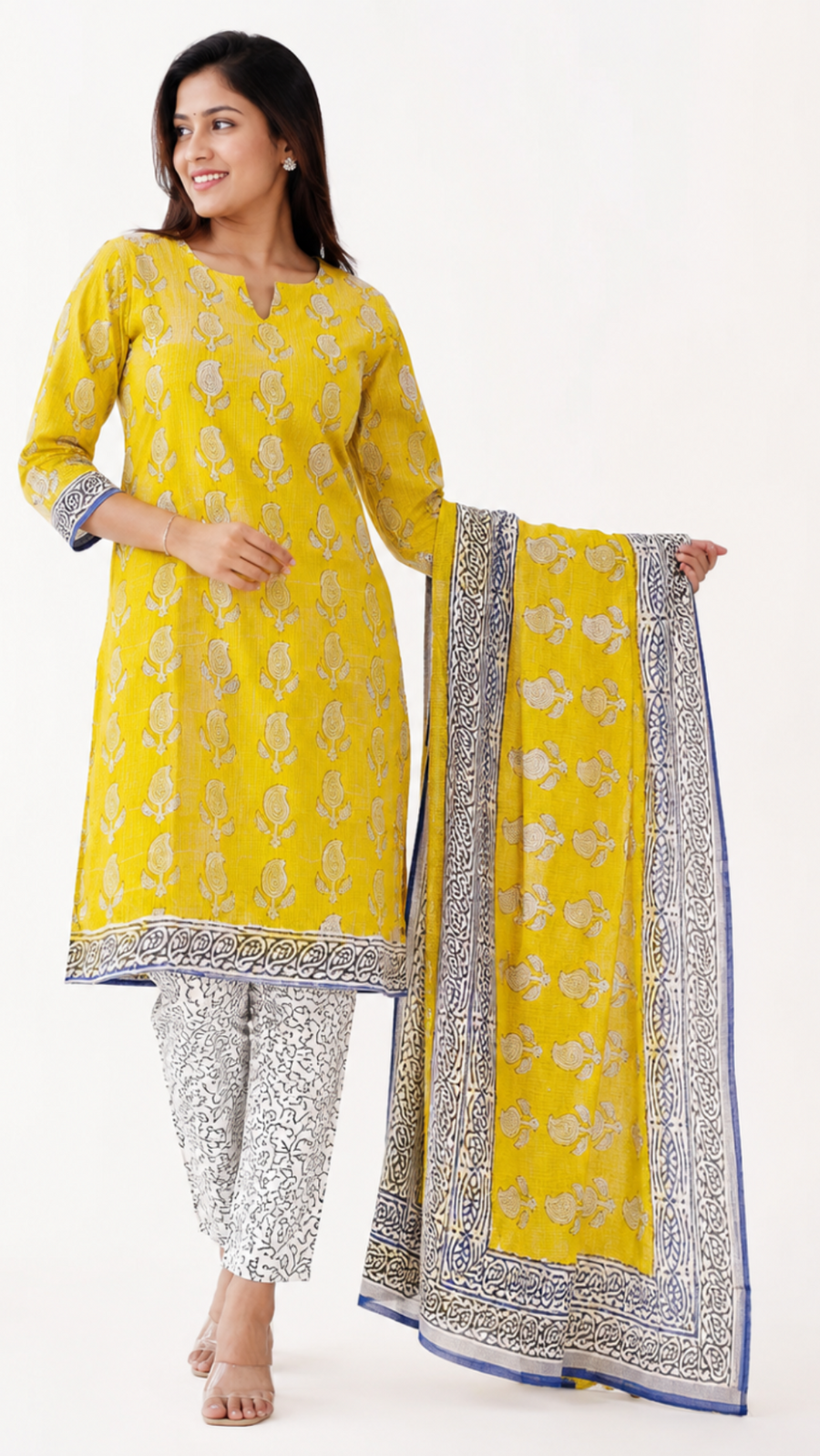 A woman models a yellow ethnic suit set featuring a kurta with floral prints, silver patterned pants, and a matching dupatta with a blue border, set against a plain white background.